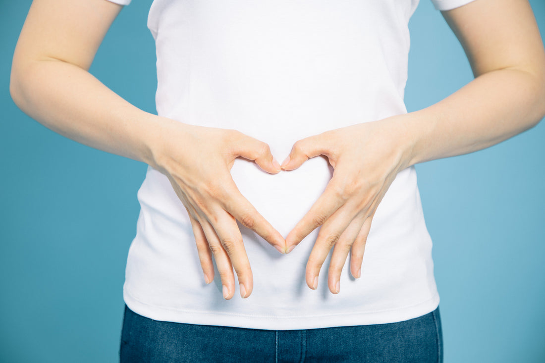 Woman in a white t-shirt using her hands to make a heart over her stomach.
