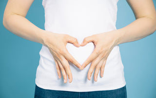 Woman in a white t-shirt using her hands to make a heart over her stomach.