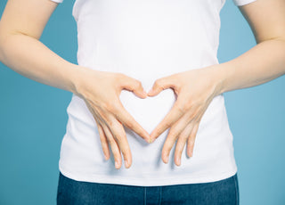 Woman in a white t-shirt using her hands to make a heart over her stomach.