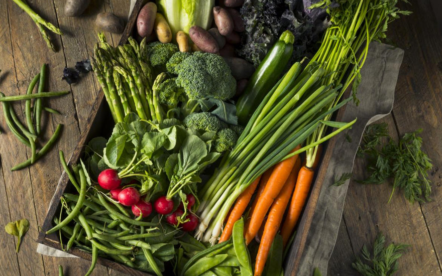 Wooden crate filled with carrots, broccoli, radishes, and other vegetables.