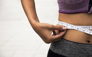 Woman in workout gear using a cloth tape measure to measure her waist.