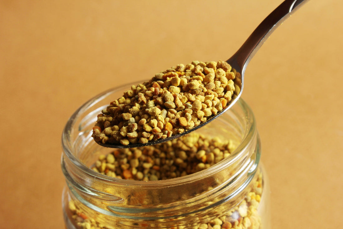 Metal spoon scooping yellow bee pollen out of a glass jar. 