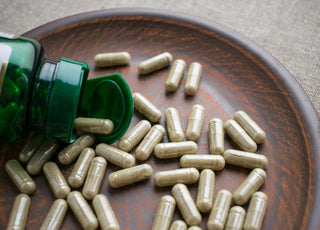 Open bottle of supplements spilling out on a wooden tray.