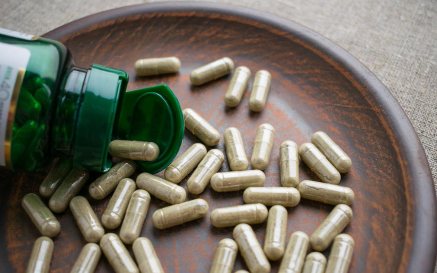 Open bottle of supplements spilling out on a wooden tray.