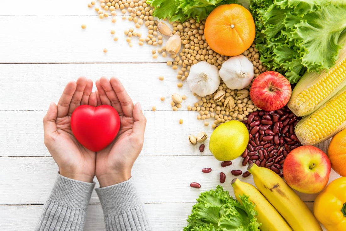 Two hands holding a red heart above fiber-loaded foods like beans, fruits, and vegetables.