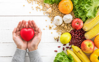 Two hands holding a red heart above fiber-loaded foods like beans, fruits, and vegetables.