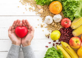 Two hands holding a red heart above fiber-loaded foods like beans, fruits, and vegetables.