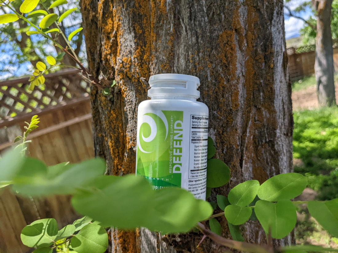 A bottle of New Earth's Defend sitting on a tree branch with green leaves.