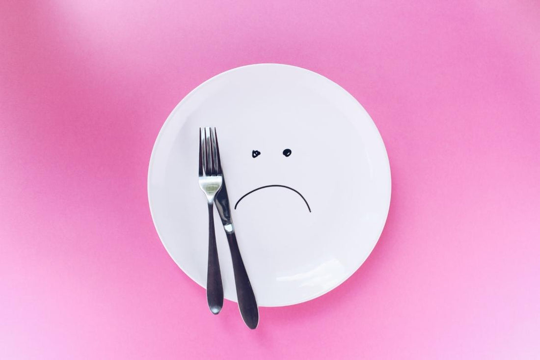 A plate with a sad face drawn on it sitting on a pink cloth with a fork and knife sitting on top of the plate.