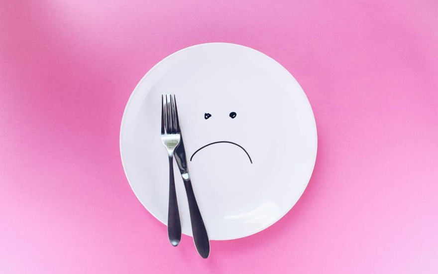 A plate with a sad face drawn on it sitting on a pink cloth with a fork and knife sitting on top of the plate.