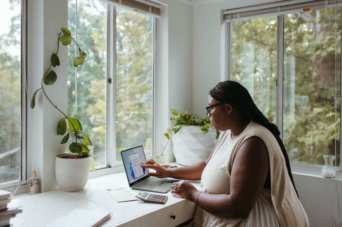 Woman sitting at a desk by a window working on her laptop.