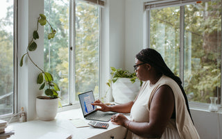 Woman sitting at a desk by a window working on her laptop.