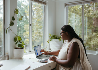 Woman sitting at a desk by a window working on her laptop.